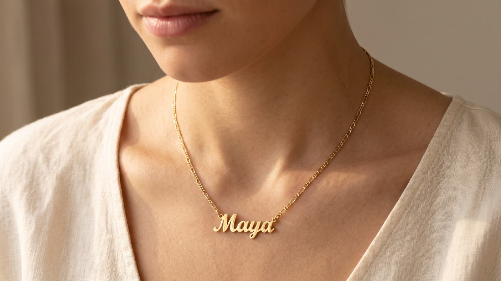 A personalized gold plated name necklace worn by a model, chin-to-collarbone crop, warm window light