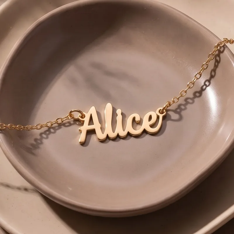 A gold plated name necklace reading “Alice” on a ceramic dish, close up