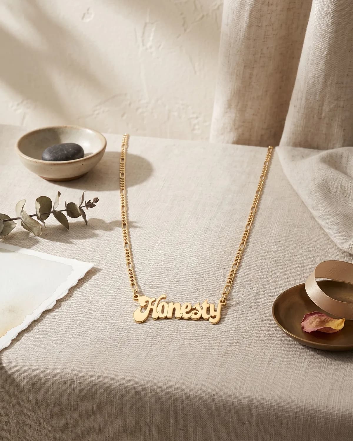 A gold plated name necklace reading “Honesty” on cream paper