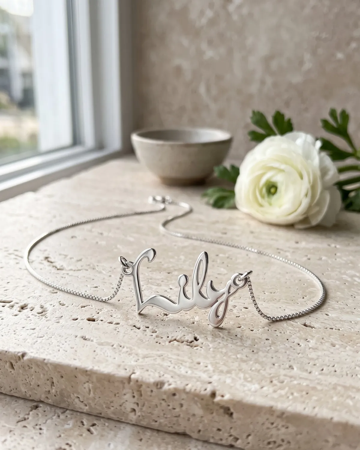 A 925 sterling silver name necklace reading “Lily” on pale travertine