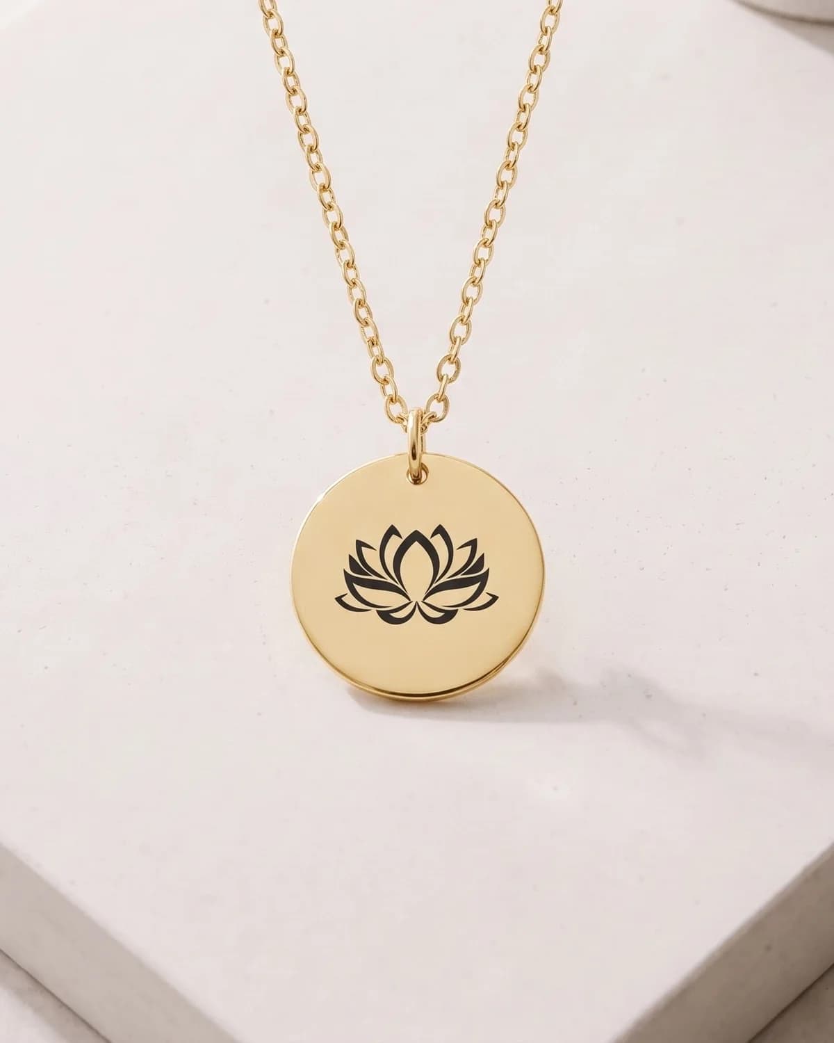 A gold plated disc pendant with a deep-engraved lotus, on a pale stone plinth