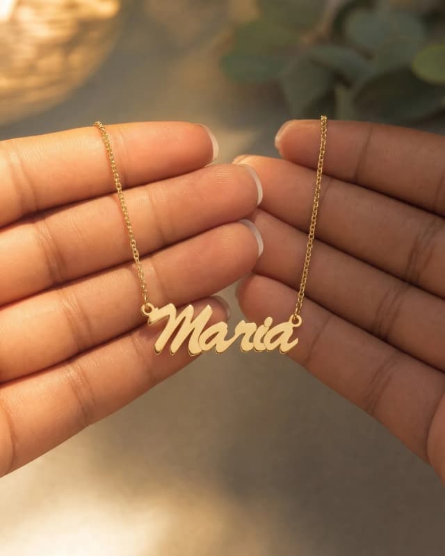 A gold plated name necklace reading “Maria” held up between two hands, a photograph made in the AI Studio
