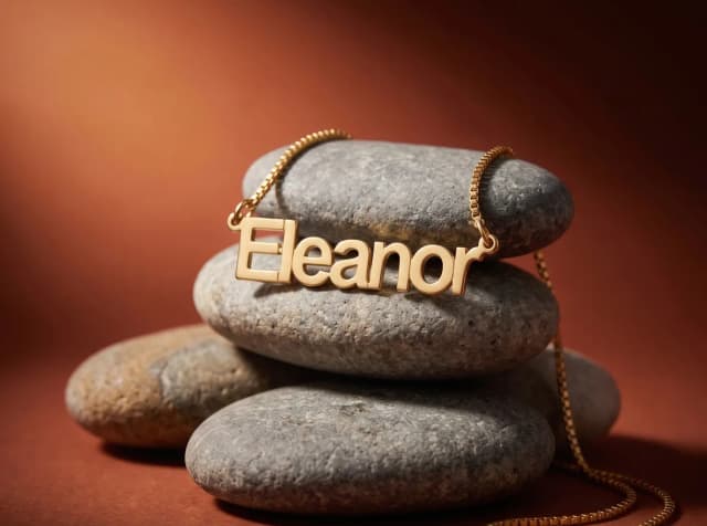 A gold plated name necklace reading “Eleanor” draped over stacked stones
