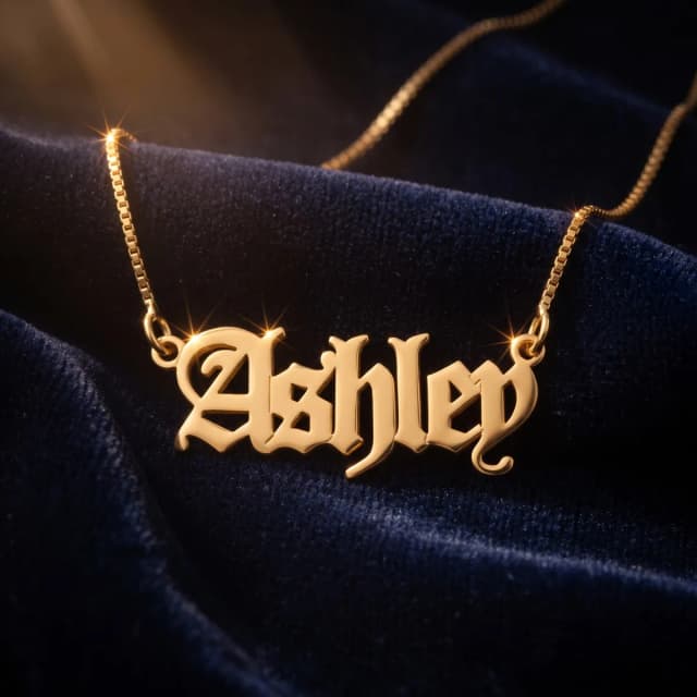 A gold plated name necklace reading “Ashley” on dark blue velvet