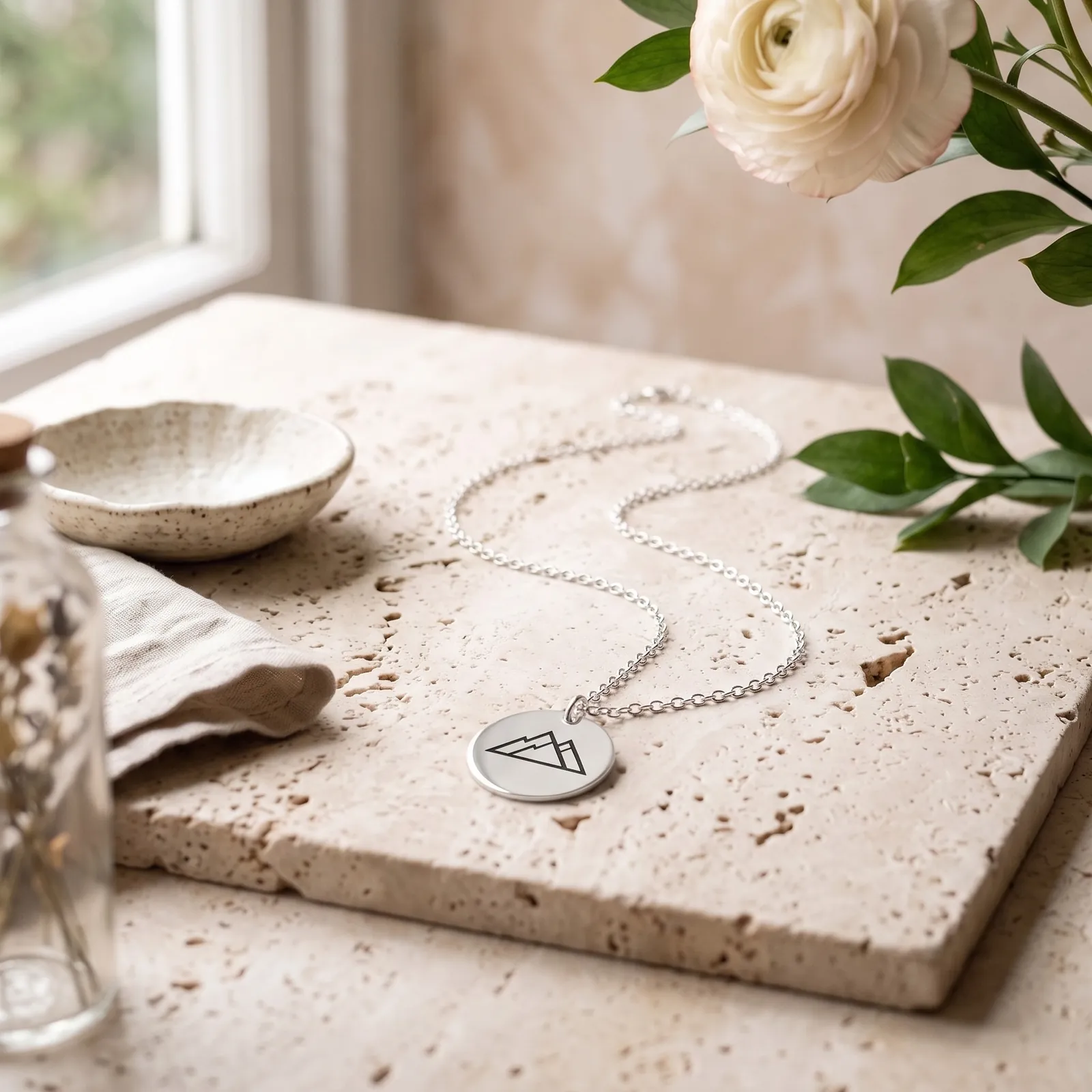 A 925 sterling silver disc necklace engraved with mountains, on pale travertine