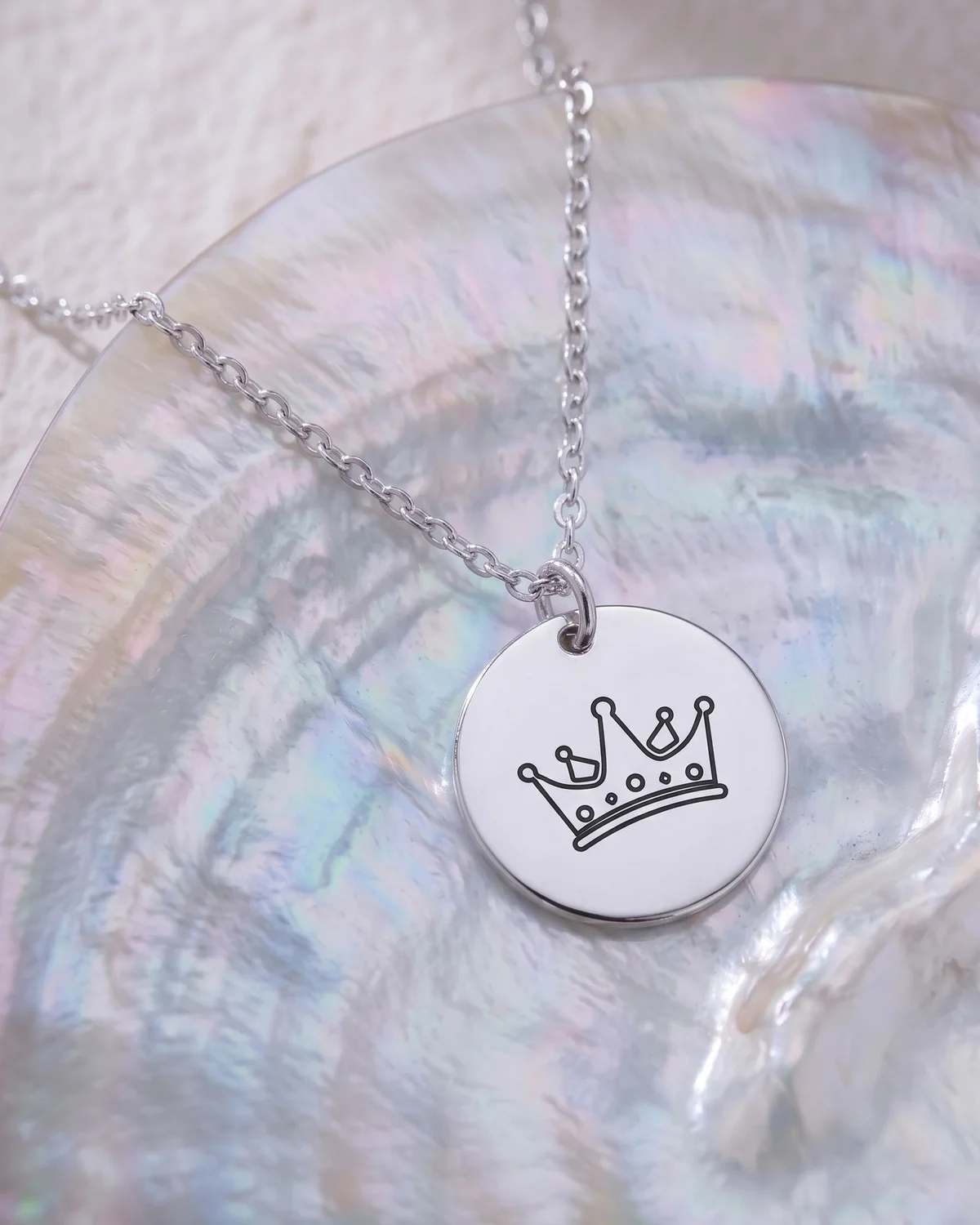 A silver plated disc pendant engraved with a crown, on a cable chain, on mother-of-pearl