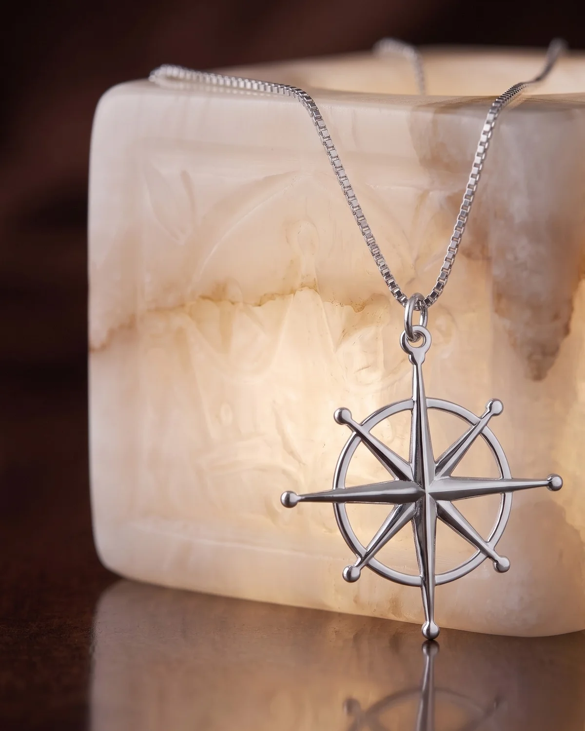 A silver plated north star pendant on a box chain, hung over a lit alabaster block