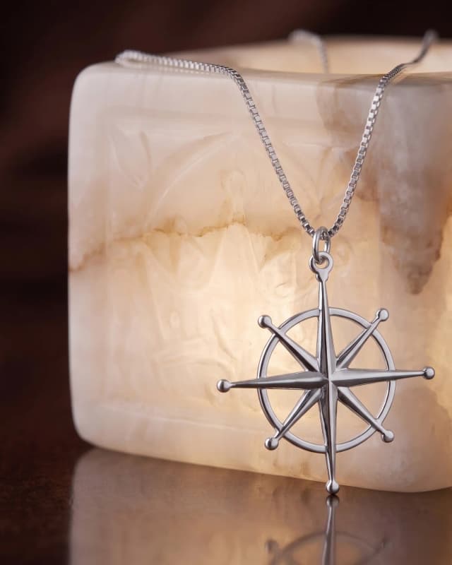 A silver plated north star pendant on a box chain, hung over a lit alabaster block