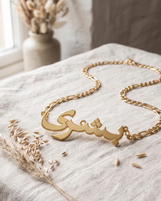 A gold plated Arabic name necklace reading “بشرى” on ivory linen